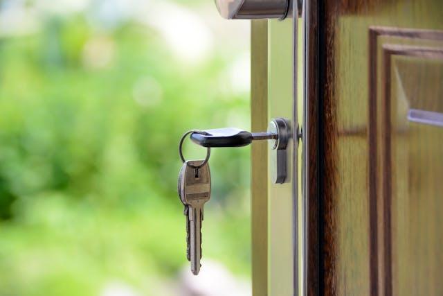 Close-up of a key inserted in a door lock, with greenery in the background