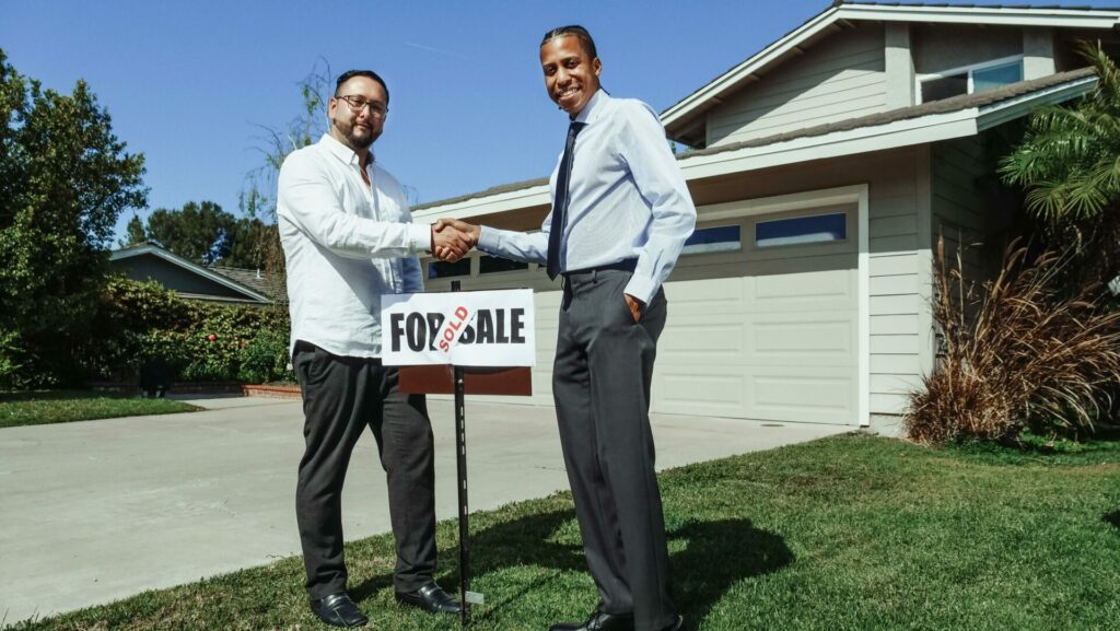Real estate agent shaking hands with buyer over the "Sold" sign